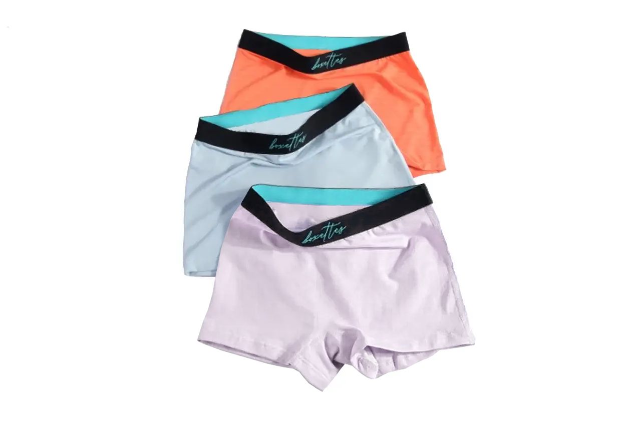 Three pairs of women's underwear in orange, light blue, and white with black waistbands on a white background.